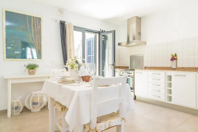 Un comedor luminoso con la mesa puesta junto a una cocina blanca.