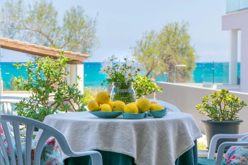 Una mesa de comedor en un patio junto al mar tiene un cuenco de limones junto al agua turquesa.