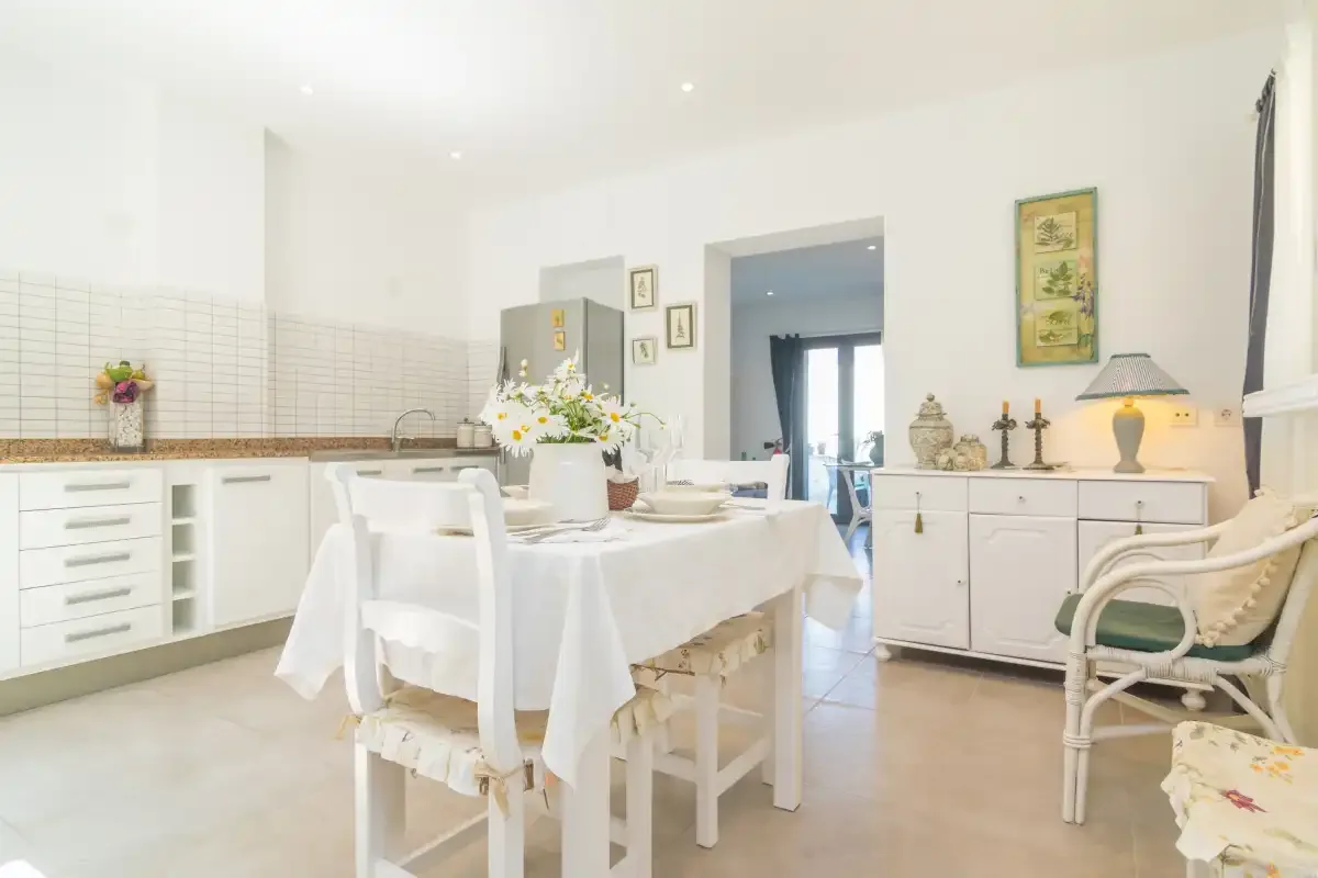 Un comedor luminoso con una mesa blanca junto a armarios de cocina empotrados.