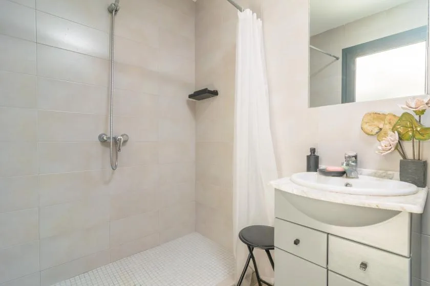 Un baño luminoso con ducha alicatada, lavabo y espejo.