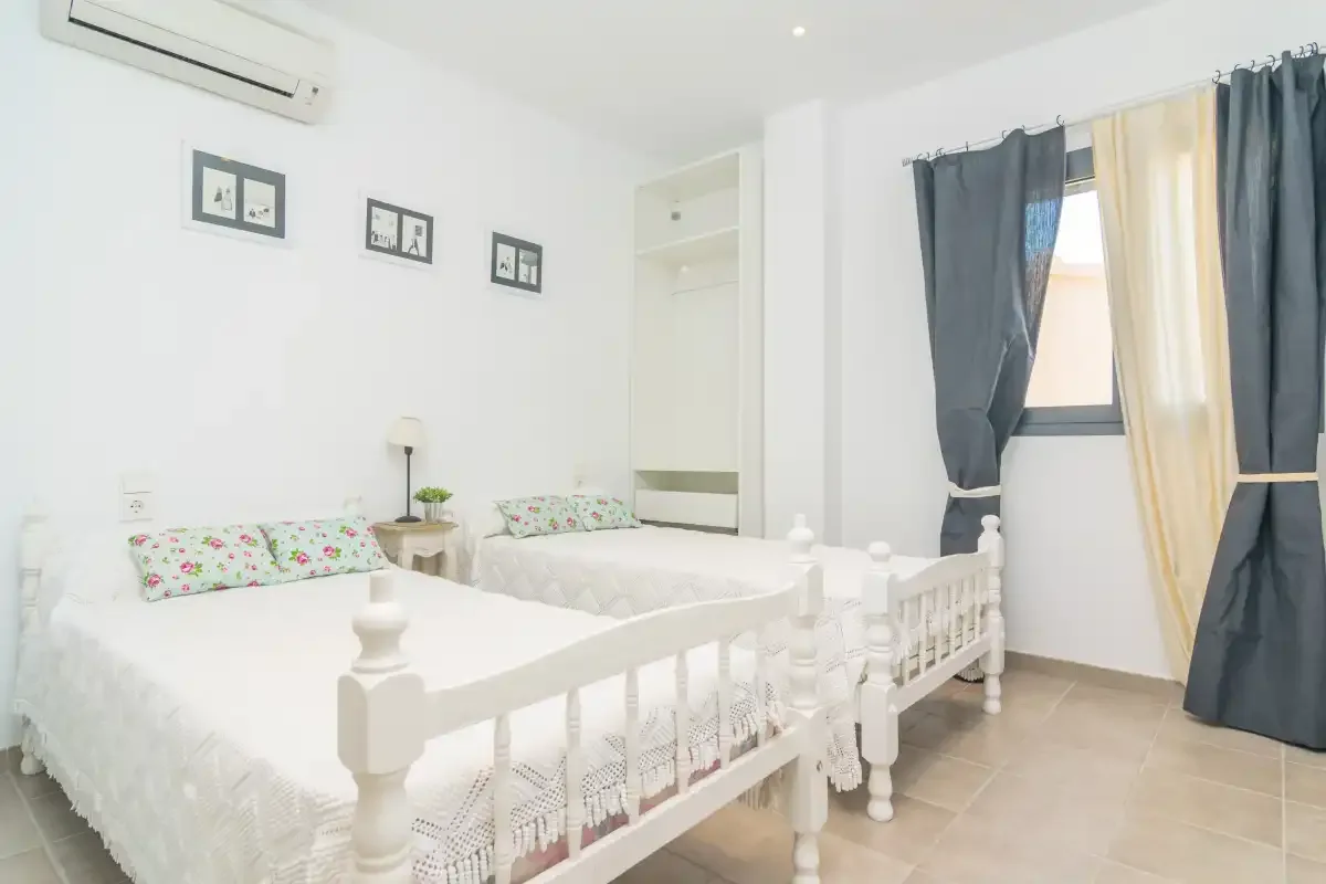 Un dormitorio luminoso con dos camas y cortinas junto a la ventana.
