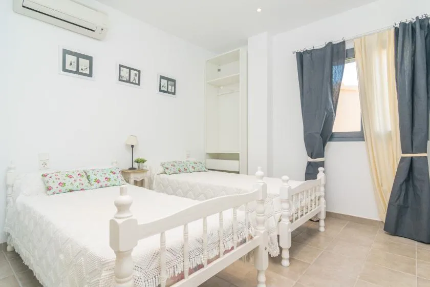 Un dormitorio luminoso con dos camas blancas y cortinas oscuras junto a la ventana.