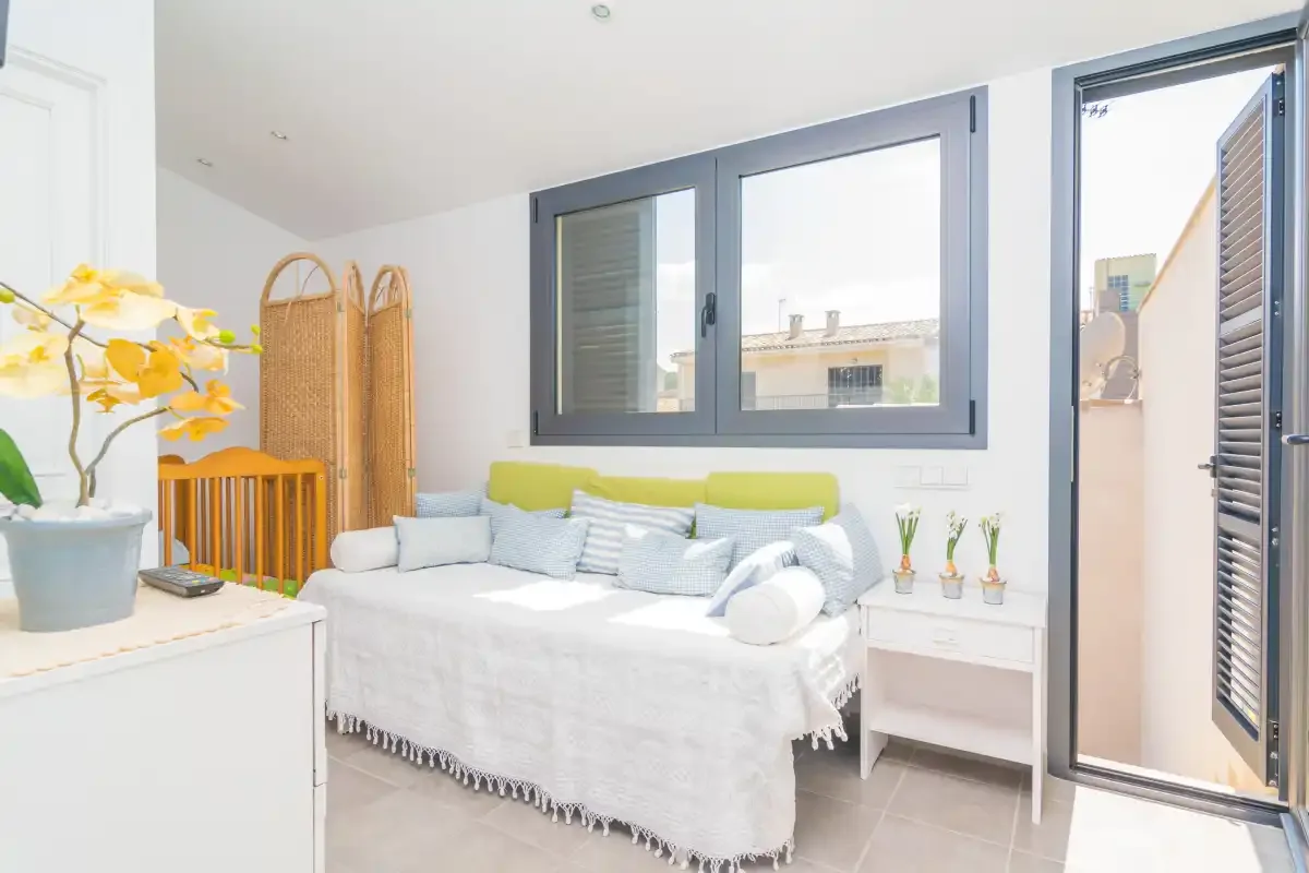 Un dormitorio luminoso con una cama blanca bajo una ventana grande.