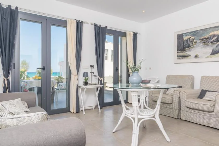 Una sala luminosa con una mesa de comedor de vidrio y asientos junto a ventanas altas.