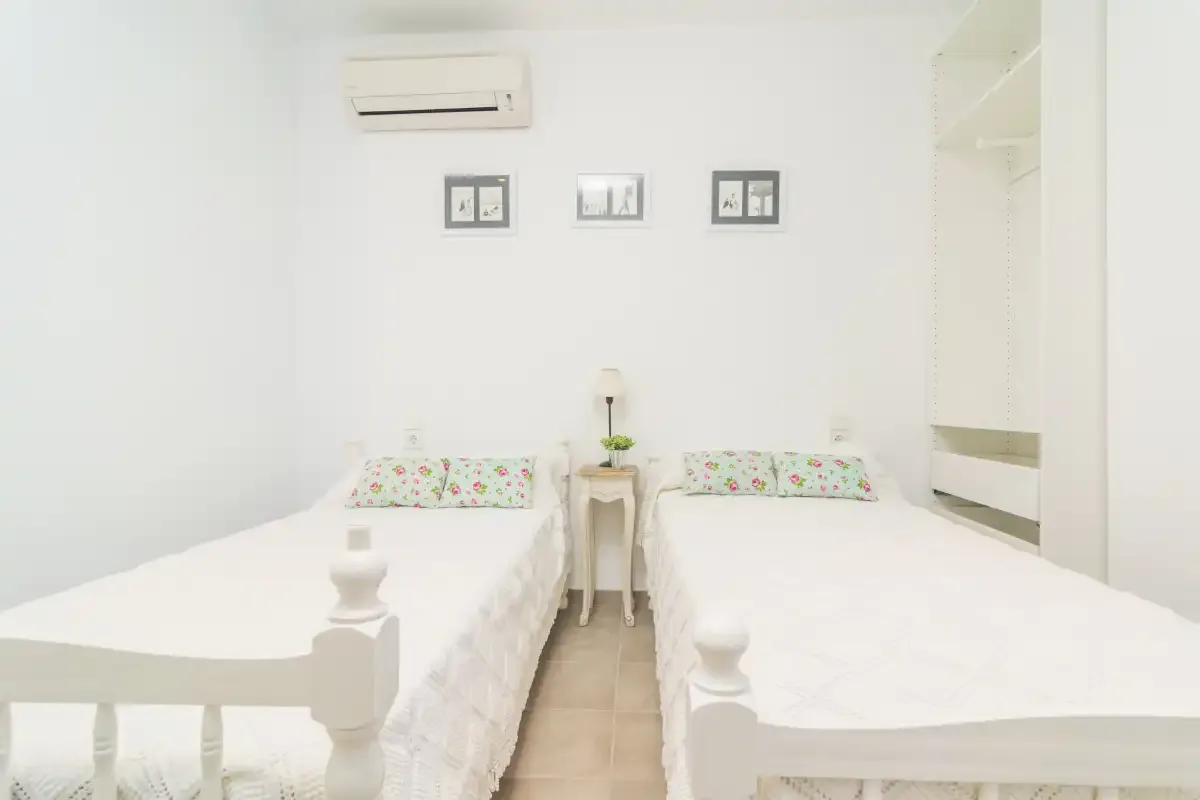 Un dormitorio luminoso con dos camas y almohadas florales.