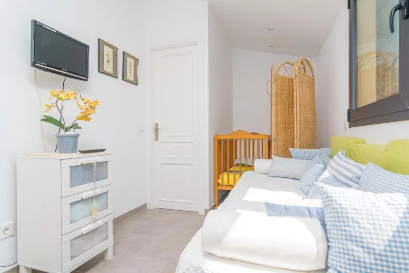 Un dormitorio luminoso con una cama, un televisor y una cuna pequeña de madera.