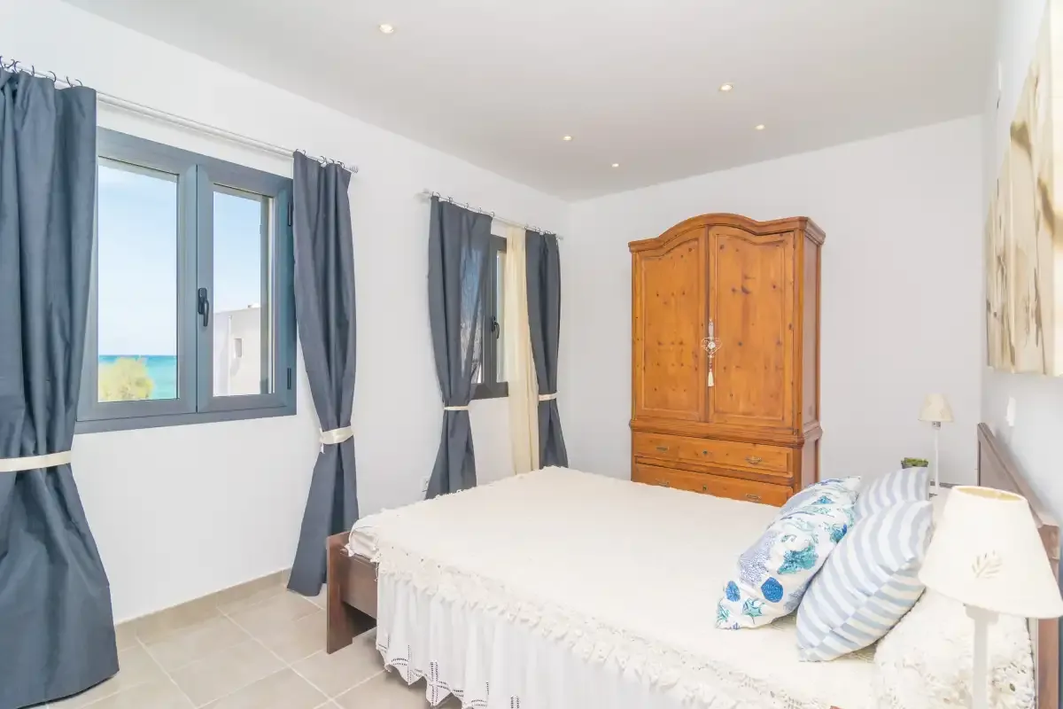 Un dormitorio con una cama, ventanas con cortinas y un armario de madera.