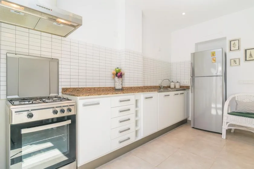Una cocina luminosa con gabinetes blancos, azulejos en la pared y electrodomésticos de acero inoxidable.