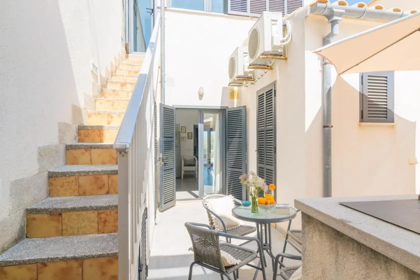 Un patio soleado tiene una mesa pequeña y sillas junto a una escalera exterior.