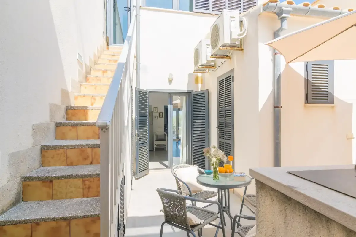 Un patio soleado con una mesa pequeña y sillas junto a una escalera exterior.