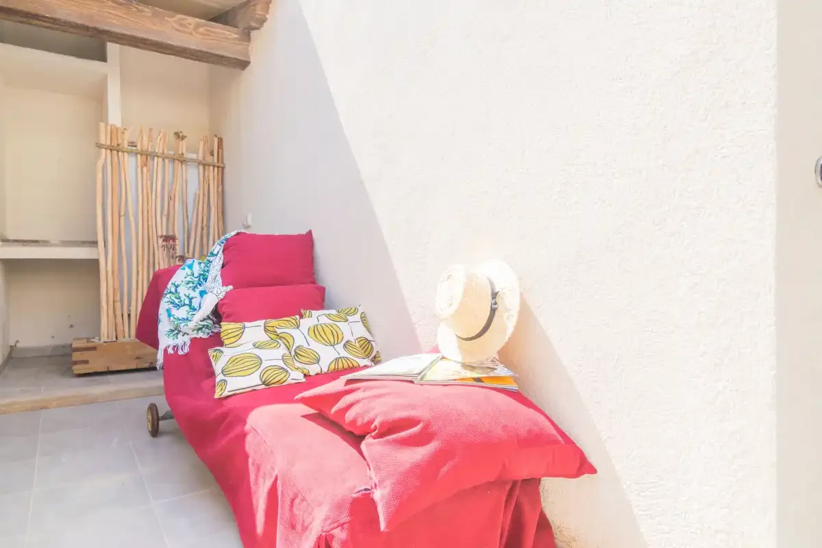 Una zona de descanso luminosa con una cama roja y un sombrero de paja encima.