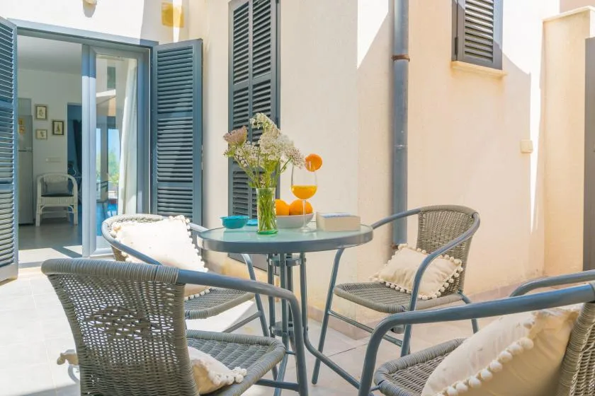 Un patio soleado tiene una mesa de vidrio y asientos tejidos.