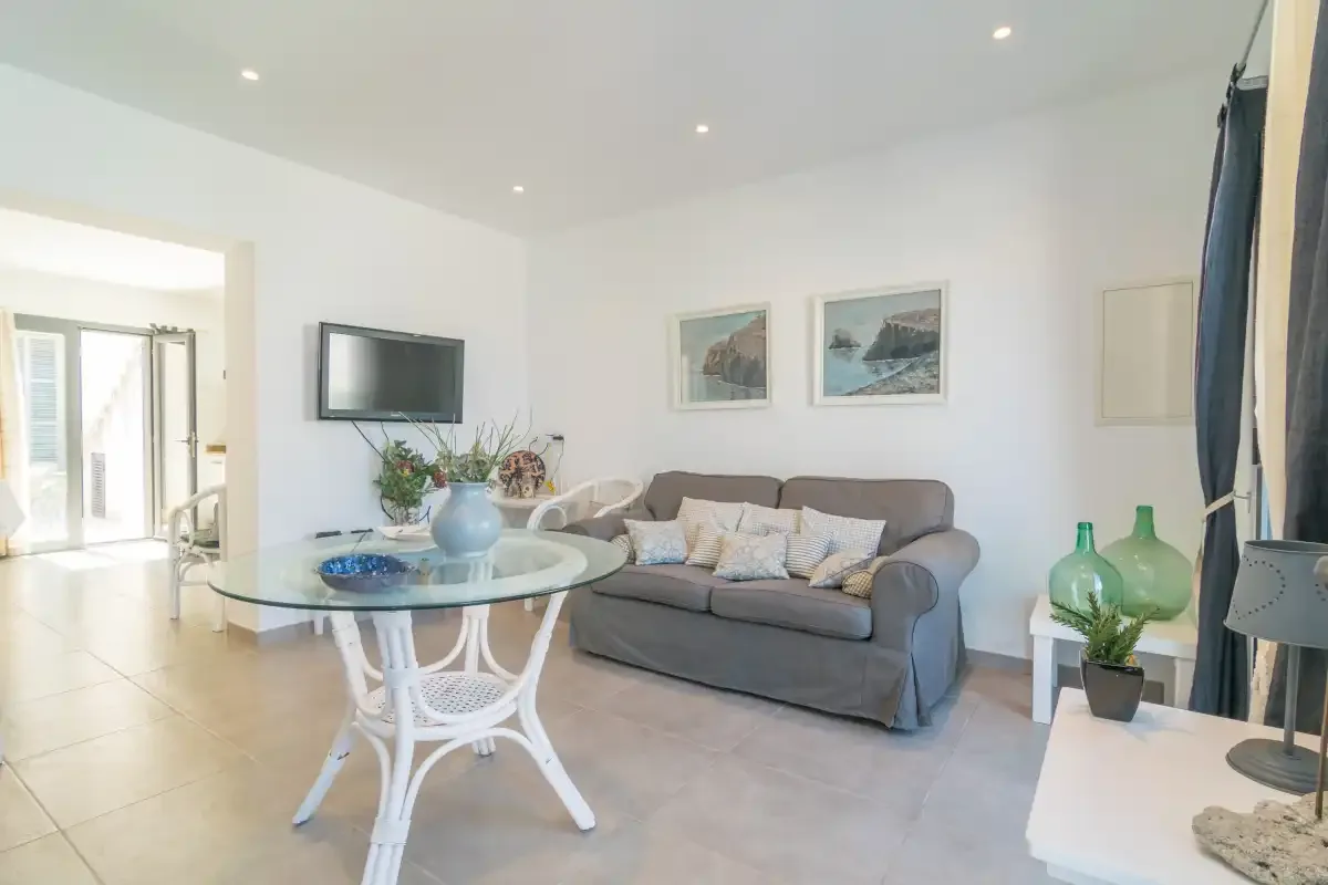 Una sala de estar luminosa con sofá, mesa de vidrio y cuadros enmarcados.