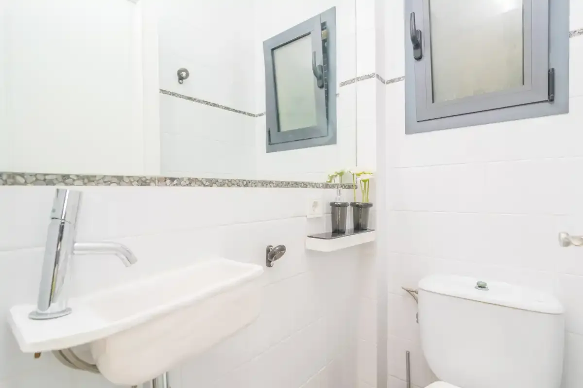 Un baño luminoso con azulejos, lavabo de pared e inodoro.