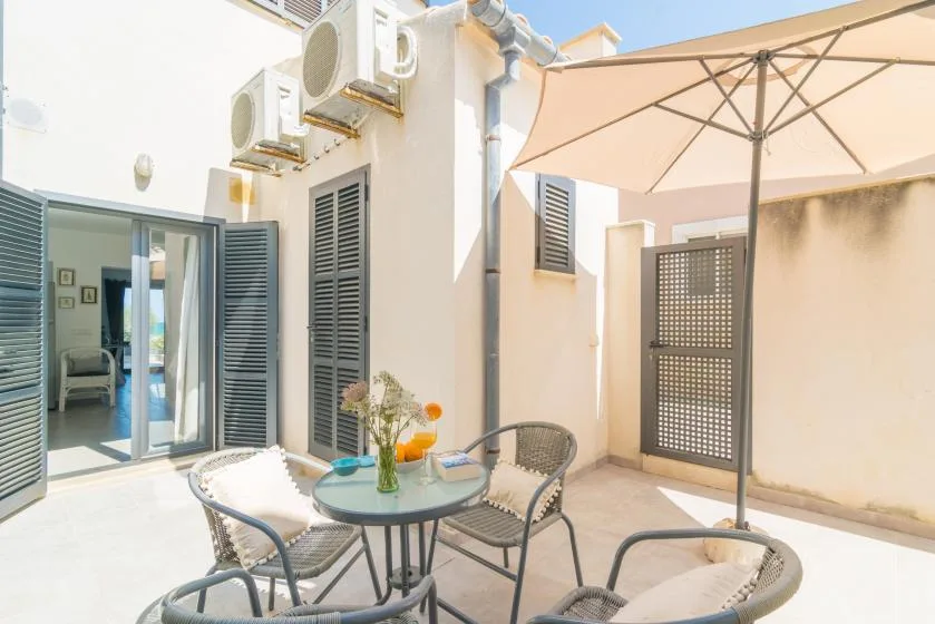 Un patio soleado tiene una mesa redonda, asientos al aire libre y una sombrilla grande.