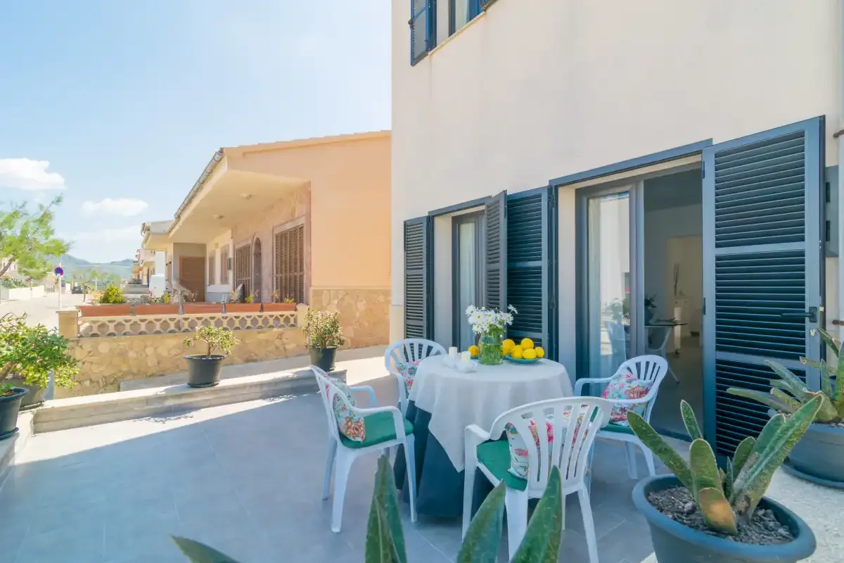 Una zona de comedor exterior junto a un edificio blanco, con mesa y sillas.