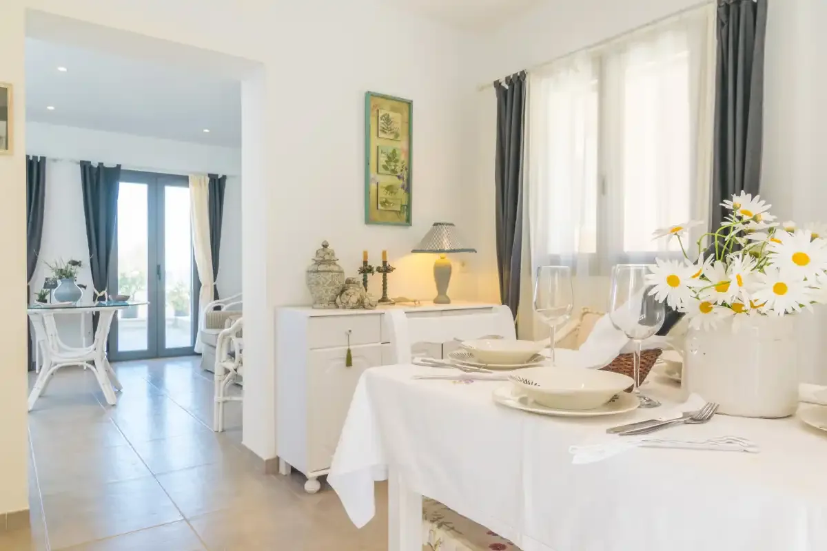 Un comedor luminoso con la mesa puesta y flores blancas junto a una ventana soleada.