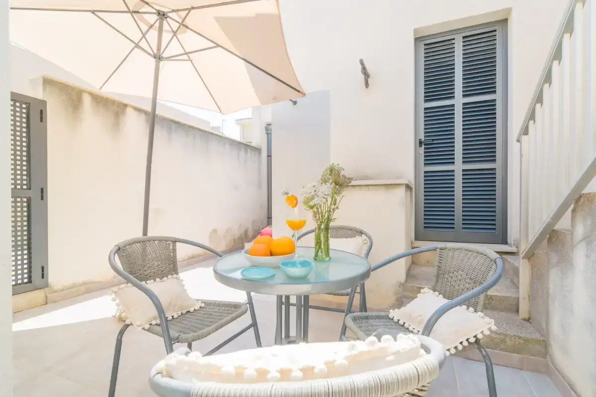 Un patio soleado con asientos alrededor de una mesa pequeña bajo una sombrilla grande.