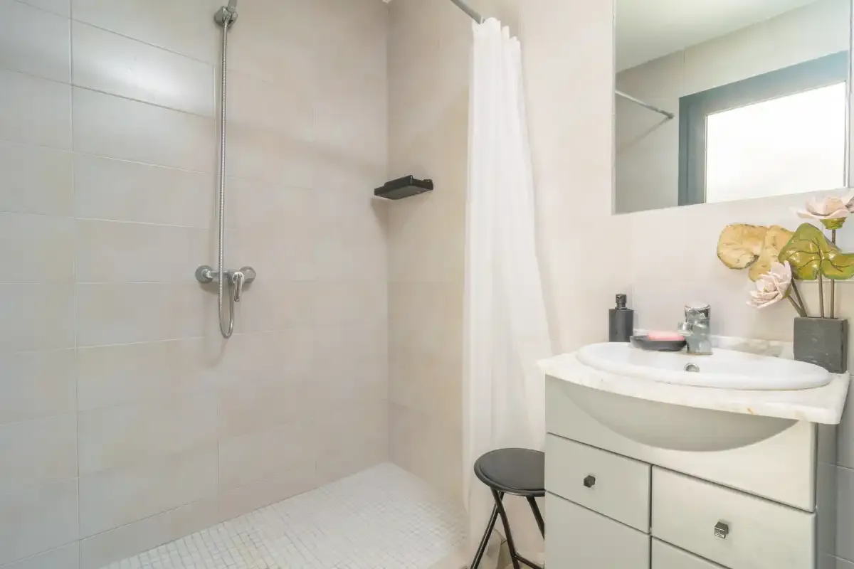Un baño con ducha revestida de azulejos y un mueble de lavabo blanco.