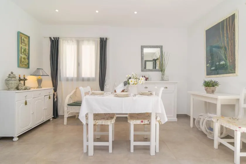 Un comedor luminoso con una mesa puesta y muebles blancos.