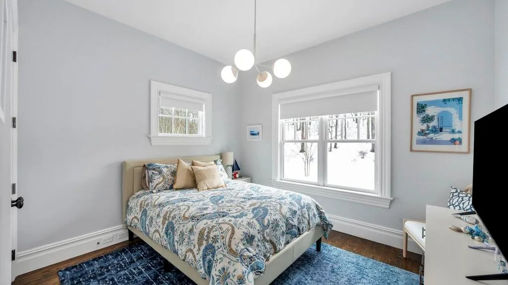 Un dormitorio luminoso con una colcha estampada, ventanas amplias y una alfombra azul.