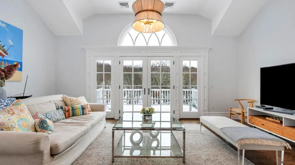 Una sala luminosa con asientos, una mesa de centro de vidrio y puertas que dan a un balcón.