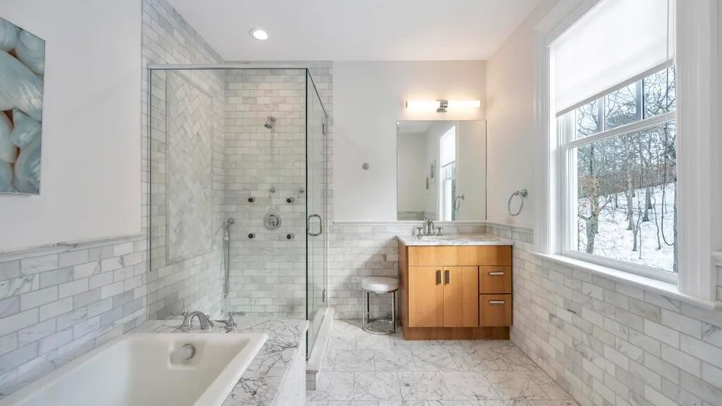 Un baño luminoso con ducha de vidrio, bañera y tocador de madera.