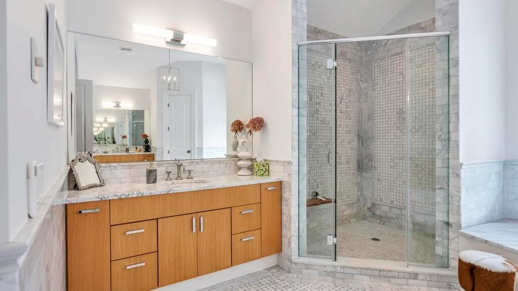 Un baño luminoso con tocador de madera, espejo amplio y ducha de vidrio.