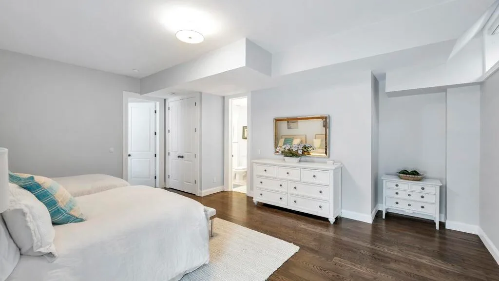 Un dormitorio luminoso con una cama, cómodas blancas y piso de madera.