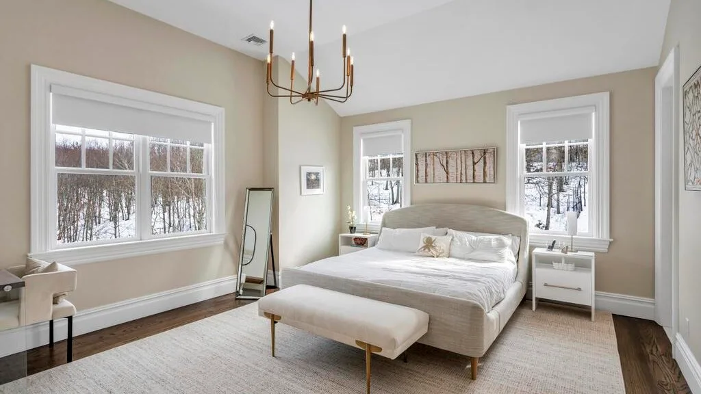 Un dormitorio luminoso con una cama grande y ventanas con vista a los árboles.