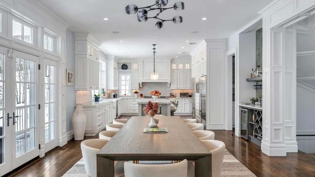 Una cocina y comedor luminosos con una mesa larga y gabinetes blancos.