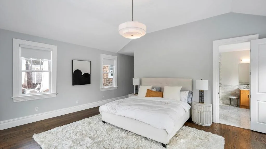 Un dormitorio luminoso con una cama, ropa de cama blanca y una alfombra suave.