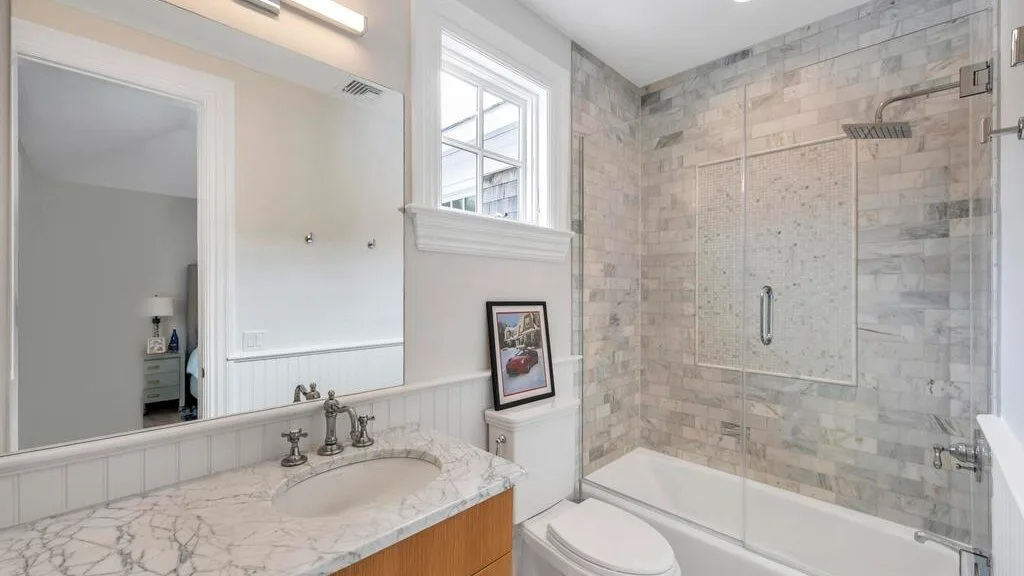 Un baño luminoso con un tocador de aspecto marmolado y una bañera con ducha revestida de azulejos.
