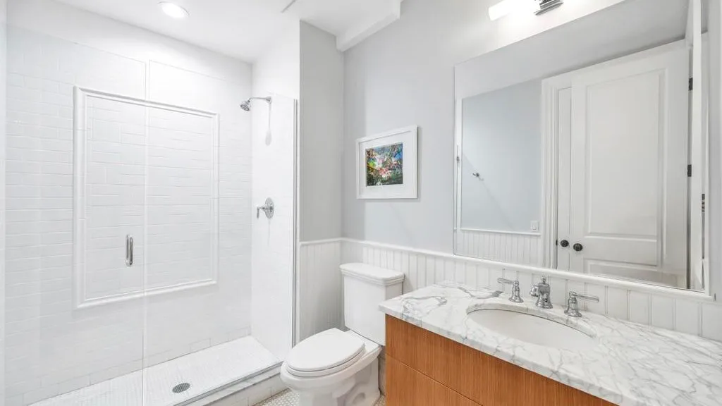 Un baño luminoso con lavabo, inodoro y ducha con mampara de vidrio.