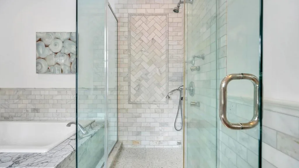 Un baño de azulejos cuenta con una ducha de vidrio junto a una bañera.