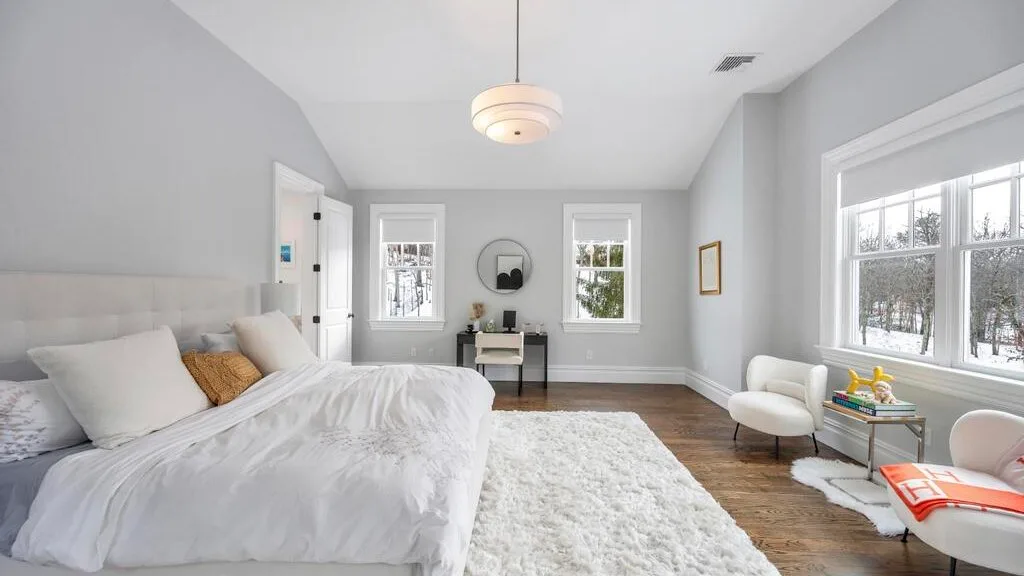 Un dormitorio luminoso con una cama grande, una alfombra blanca y ventanas.
