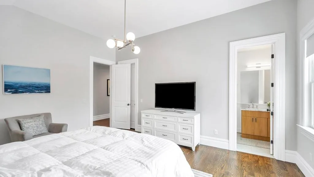 Un dormitorio luminoso con una cama bien hecha y un televisor sobre una cómoda.