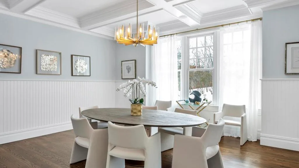 Un comedor luminoso con una mesa redonda, asientos y grandes ventanas.