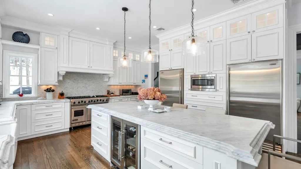 Una cocina blanca y luminosa con una isla grande y electrodomésticos de acero inoxidable.