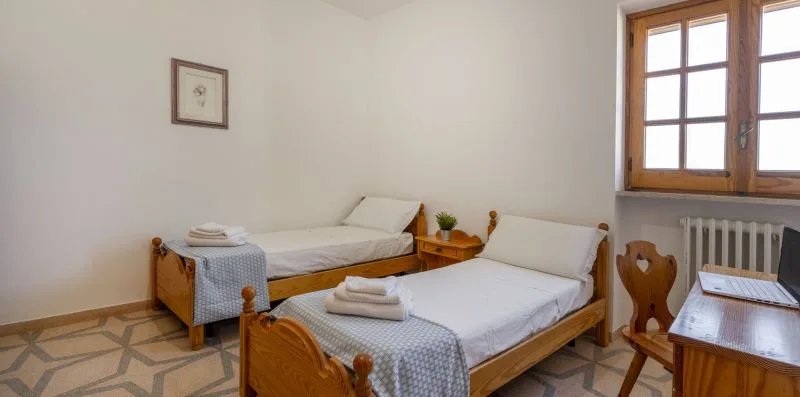 A bedroom with two single beds, folded towels, and a wooden-framed window.