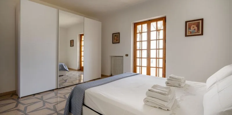 Un dormitorio con una cama bien tendida junto a una ventana grande.