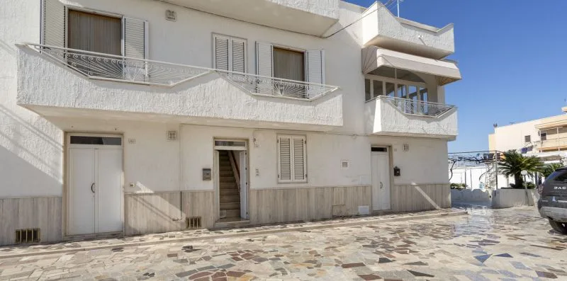 Un edificio blanco de varias plantas con balcones da a una zona exterior pavimentada.