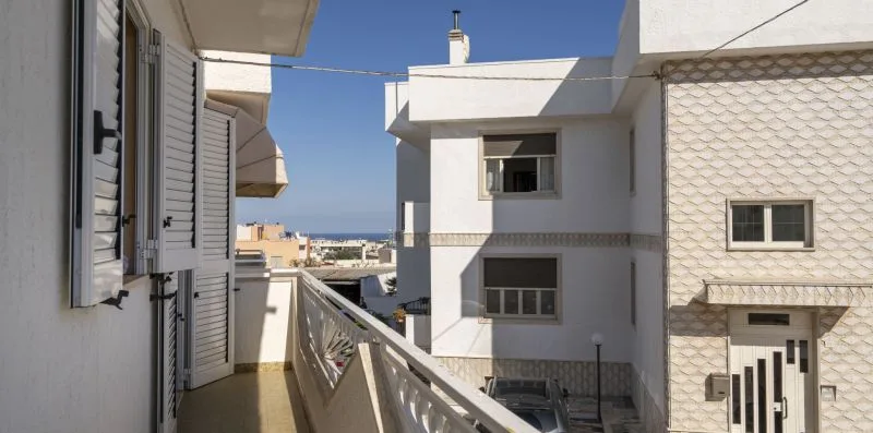 Un balcón soleado da a edificios cercanos bajo un cielo azul despejado.