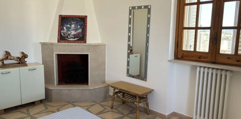 Una habitación luminosa con chimenea, espejo alto y ventana con marco de madera.