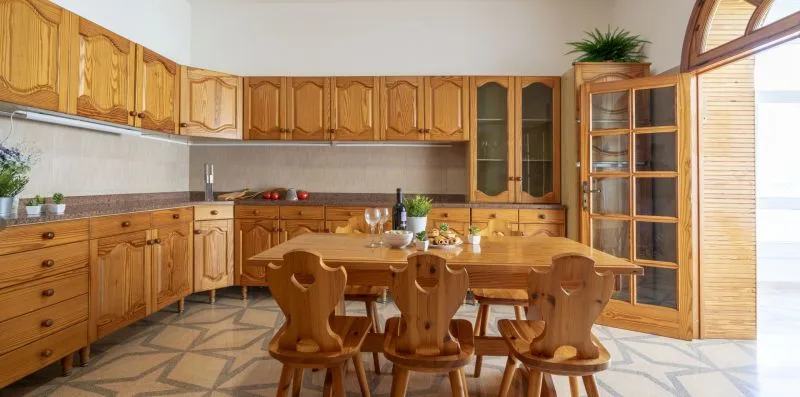 Una mesa de comedor de madera y sillas están en una cocina con amplios armarios de madera.