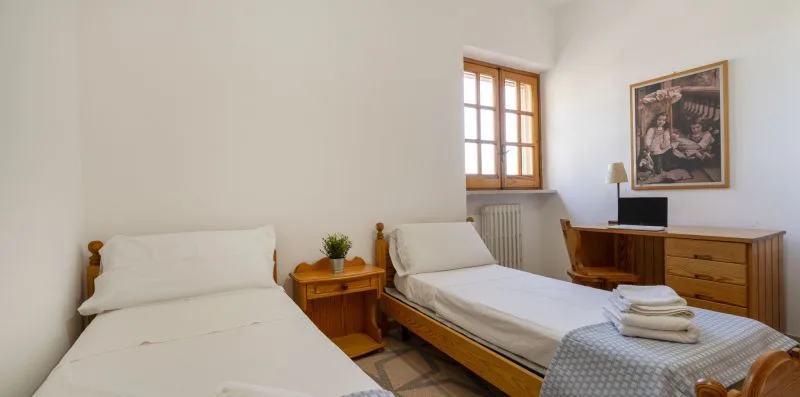 Un dormitorio luminoso con dos camas, una cómoda de madera y una ventana.