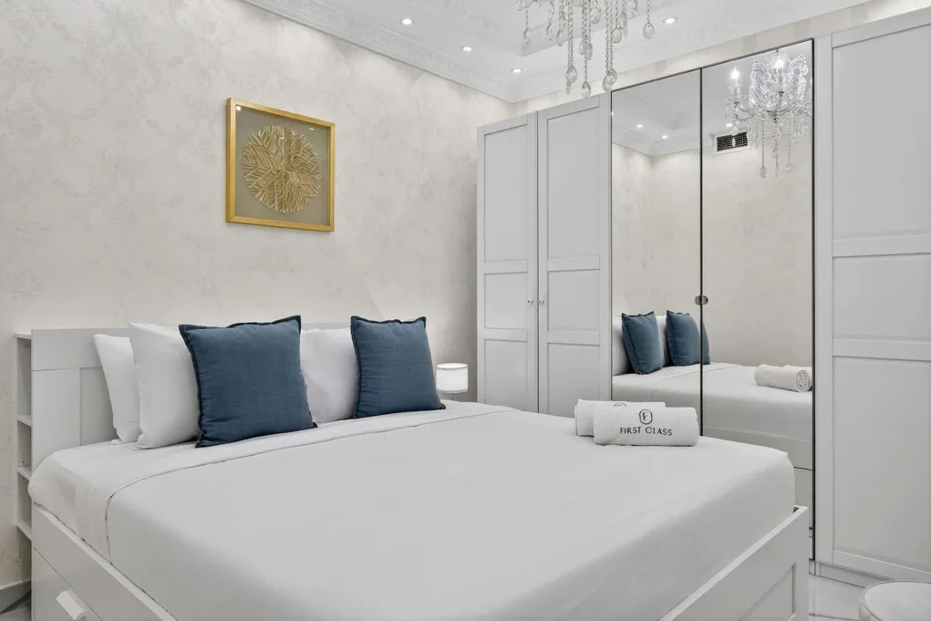 Un dormitorio con ropa de cama blanca, cojines azules y puertas de armario con espejo.