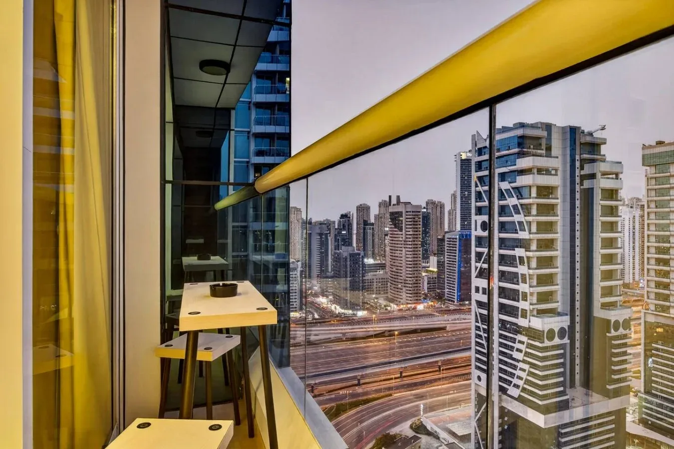 Una zona de estar en un balcón da a un horizonte urbano y una vía elevada.