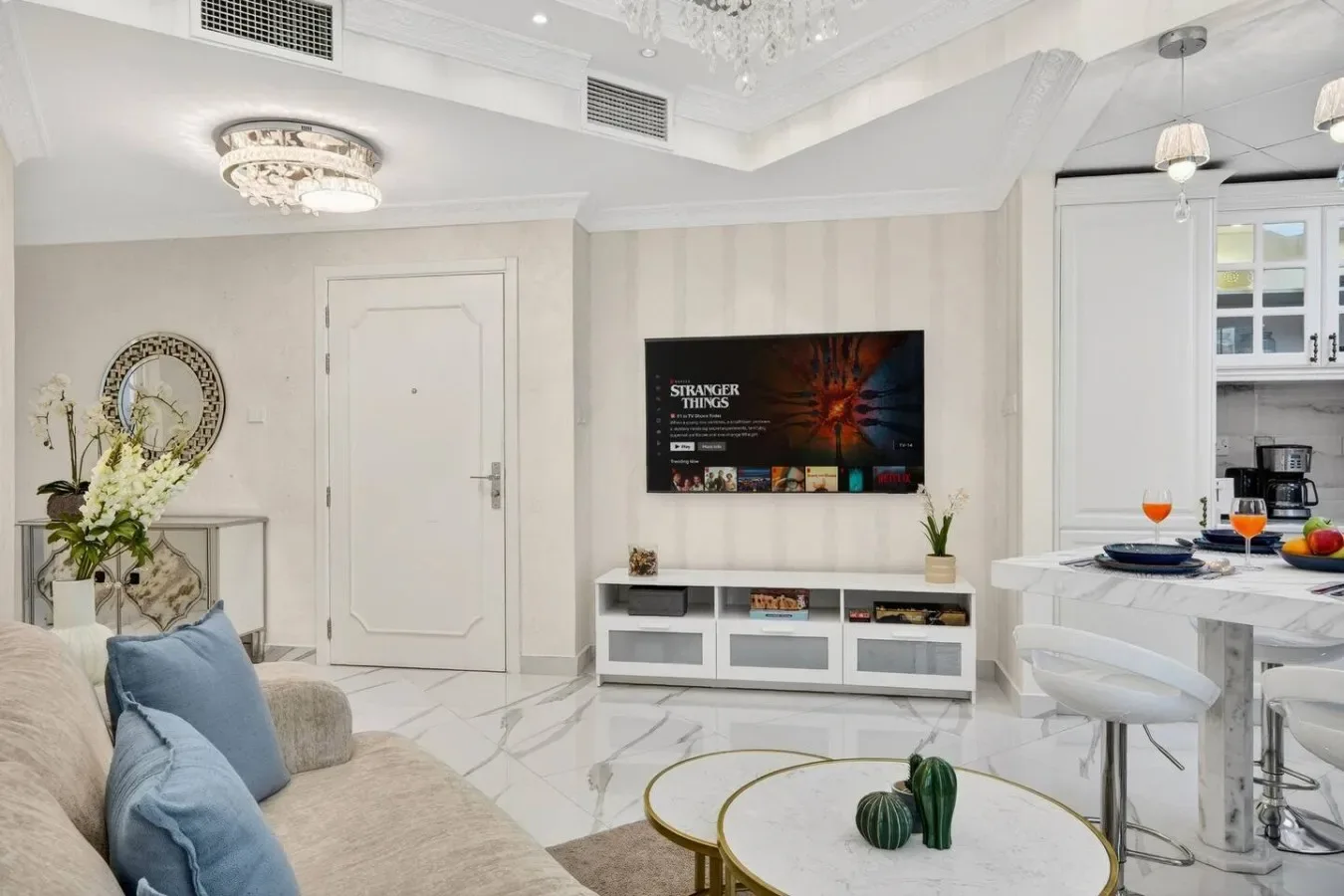 Una luminosa sala de estar con asientos, un televisor en la pared y una cocina contigua.
