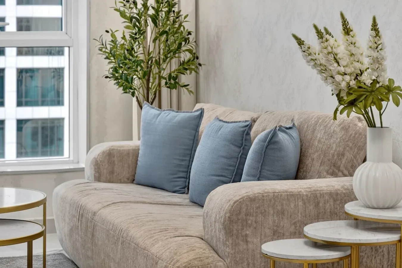 Una sala de estar con un sofá beige y cojines azules junto a una ventana.